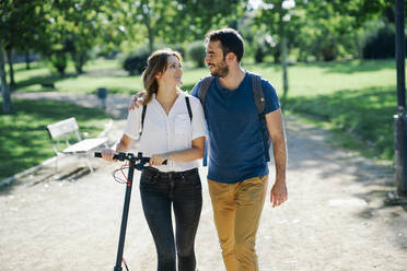 Happy couple with electric scooter in a city park - JSMF01320