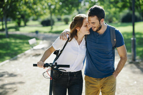 Glückliches Paar mit Elektroroller in einem Stadtpark - JSMF01322