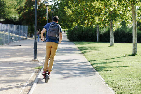 Back view of man with backpack riding electric scooter stock photo