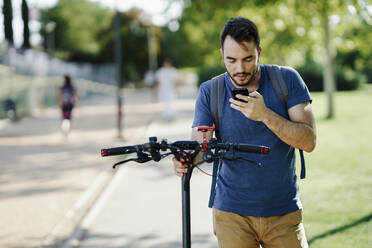 Portrait of man with electric scooter using cell phone - JSMF01329