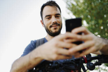 Porträt eines zufriedenen Mannes mit Elektroroller, der auf sein Mobiltelefon schaut - JSMF01331