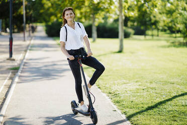 Portrait of content woman with electric scooter - JSMF01335