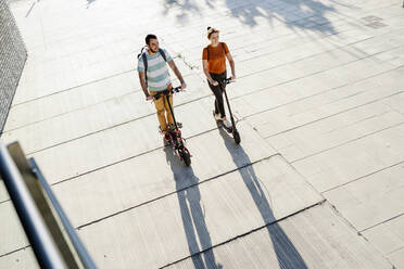 Couple with backpacks riding electric scooters - JSMF01339