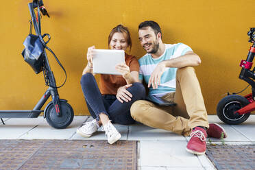 Portrait of smiling couple with electric scooters using digital tablet - JSMF01341