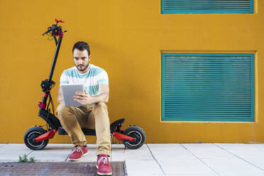 Portrait of man sitting on electric scooter using digital tablet - JSMF01345