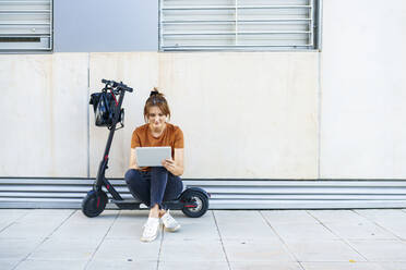 Porträt einer Frau, die auf einem Elektroroller sitzt und ein digitales Tablet benutzt - JSMF01347
