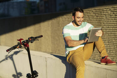 Portrait of smiling man with electric scooter using digital tablet - JSMF01351