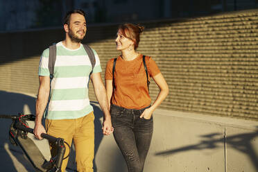 Portrait of happy couple walking hand in hand at sunlight - JSMF01354