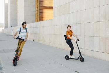 Couple riding electric scooters on pavement - JSMF01356