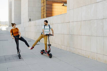 Happy couple with electric scooters in the city - JSMF01357