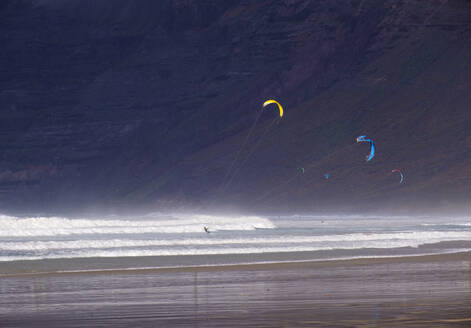 Spanien, Kanarische Inseln, Caleta de Famara, Kiteboarder am Playa de Famara mit hoher Klippe im Hintergrund - SIEF09187