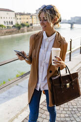 Lächelnde Frau mit Kaffee zum Mitnehmen und Smartphone in der Stadt - GIOF07308