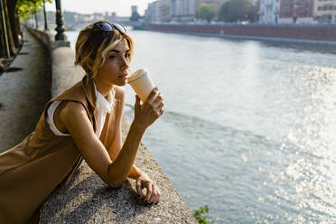 Woman drinking coffee at riverside in the city - GIOF07312