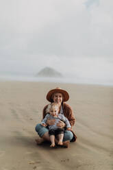 Mutter und Kleinkind sitzen am Strand, Morro Bay, Kalifornien, Vereinigte Staaten - ISF22337