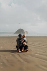 Vater und Kleinkind sitzen am Strand, Morro Bay, Kalifornien, Vereinigte Staaten - ISF22339