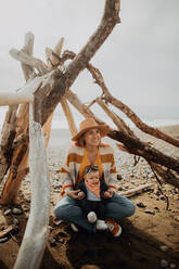 Mother and baby sitting inside wickiup on beach - ISF22350