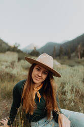 Young woman in stetson sitting in rural valley, portrait, Mineral King, California, USA - ISF22370