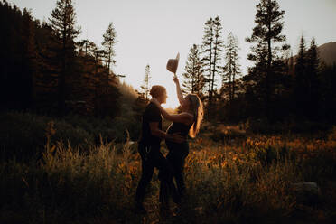 Pregnant mid adult couple holding up stetson in rural valley at sunset, Mineral King, California, USA - ISF22377