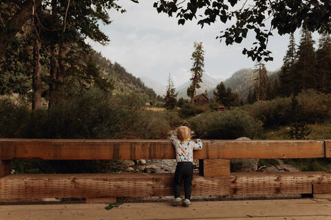 Weibliches Kleinkind, das von einer ländlichen Brücke auf den Fluss schaut, Rückansicht, Mineral King, Kalifornien, USA, lizenzfreies Stockfoto
