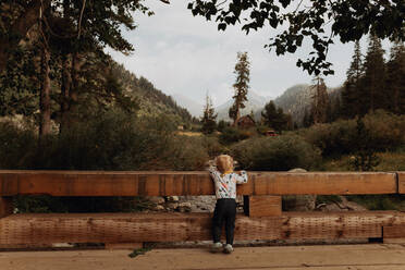 Weibliches Kleinkind, das von einer ländlichen Brücke auf den Fluss schaut, Rückansicht, Mineral King, Kalifornien, USA - ISF22380