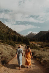 Zwei Frauen in Maxikleidern schlendern auf einer ländlichen Talstraße, Rückansicht, Mineral King, Kalifornien, USA - ISF22382