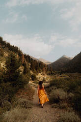 Woman in orange maxi dress strolling on rural valley dirt track, rear view, Mineral King, California, USA - ISF22385