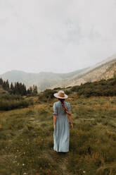 Junge Frau in Stetson und Maxikleid beim Spaziergang in einem ländlichen Tal, Rückansicht, Mineral King, Kalifornien, USA - ISF22386