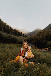 Female toddler sitting on mother's lap by rural river, portrait, Mineral King, California, USA - ISF22405
