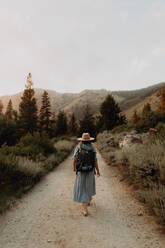 Junge Frau im Maxikleid und mit Rucksack auf der Landstraße, Rückansicht, Mineral King, Kalifornien, USA - ISF22412