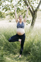 Junge schwangere Frau macht Yoga-Übungen in der Natur auf einer grünen Wiese - HMEF00641