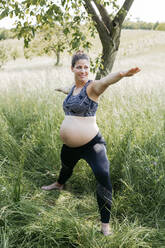 Junge schwangere Frau macht Yoga-Übungen in der Natur auf einer grünen Wiese - HMEF00642