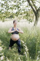 Junge schwangere Frau macht Yoga-Übungen in der Natur auf einer grünen Wiese - HMEF00643