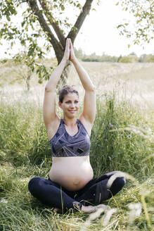 Junge schwangere Frau macht Yoga-Übungen in der Natur auf einer grünen Wiese - HMEF00644