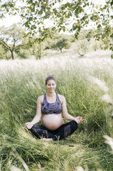 Junge schwangere Frau macht Yoga-Übungen in der Natur auf einer grünen Wiese - HMEF00645