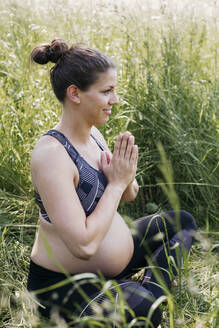 Junge schwangere Frau macht Yoga-Übungen in der Natur auf einer grünen Wiese - HMEF00646