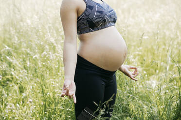 Junge schwangere Frau macht Yoga-Übungen in der Natur auf einer grünen Wiese - HMEF00647
