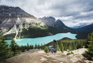 Frau sitzt auf einem Felsen mit Blick auf den Peyto-See in den Rocky Mountains. - CAVF65668