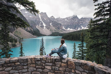 Frau sitzt auf einer Felswand und blickt auf den Moraine Lake und die Berge. - CAVF65672