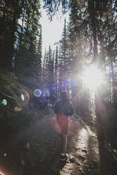 Teen boy hiking up a sunlit path in the forest in the Rocky Mountains. - CAVF65677