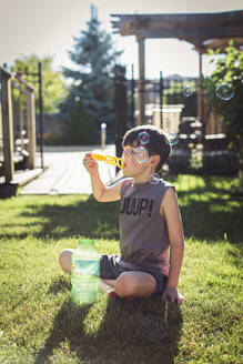 Young boy blowing bubbles in a backyard on a summer day. - CAVF65696