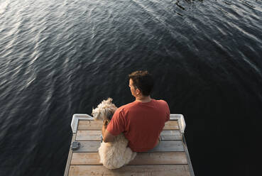 Draufsicht auf einen Mann und seinen Hund, die auf einem Steg an einem See sitzen. - CAVF65697