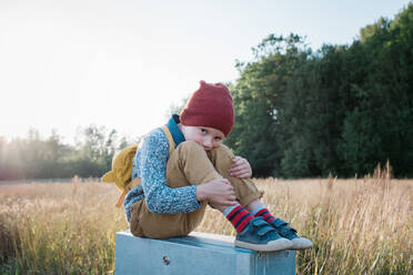 Young school boy sitting on a post whilst walking home from school - CAVF65733