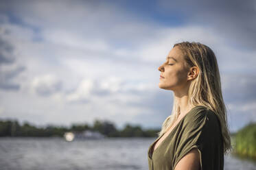 Frau mit geschlossenen Augen an einem See stehend - BFRF02126