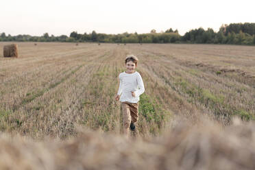 Lächelnder Junge läuft über ein Stoppelfeld - EYAF00625