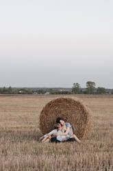 Woman with two kids sitting near a haystack on a stubble field - EYAF00629