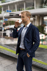 Young businessman with coffee to go in Bangkok during a rainy day - MAUF03002