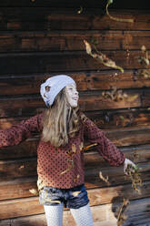 Smiling girl standing in front of a wooden wall outdoors - HMEF00654