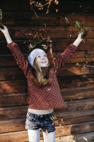 Smiling girl standing in front of a wooden wall with arms outstretched outdoors stock photo