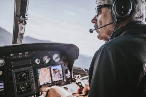 Ein Mann im Babyboomer-Alter genießt das Fliegen mit dem Hubschrauber in den Bergen. - CAVF65753