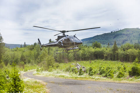 Landung eines Hubschraubers auf einer Schotterstraße im Wald., lizenzfreies Stockfoto